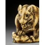 TOMOTADA: A FINE IVORY NETSUKE OF A WOLF WITH HAUNCH OF VENISON