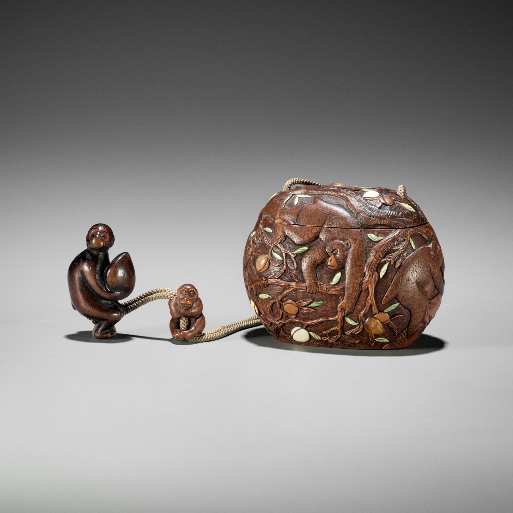 SHUOSAI: AN INLAID WOOD TONKOTSU DEPICTING MONKEYS AND PEACHES WITH EN-SUITE NETSUKE AND OJIME