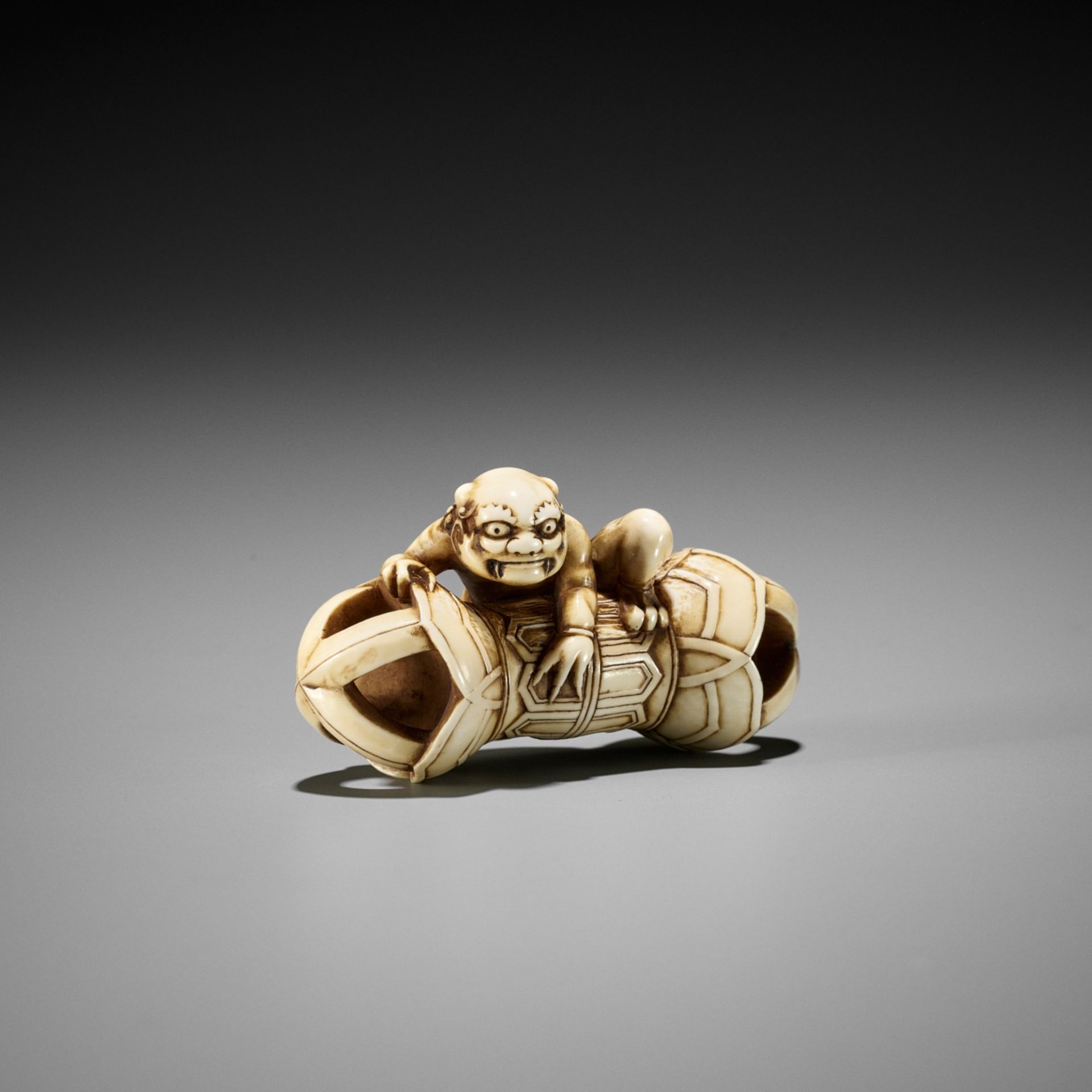 A RARE IVORY NETSUKE OF AN ONI ON A KONGO (VAJRA)