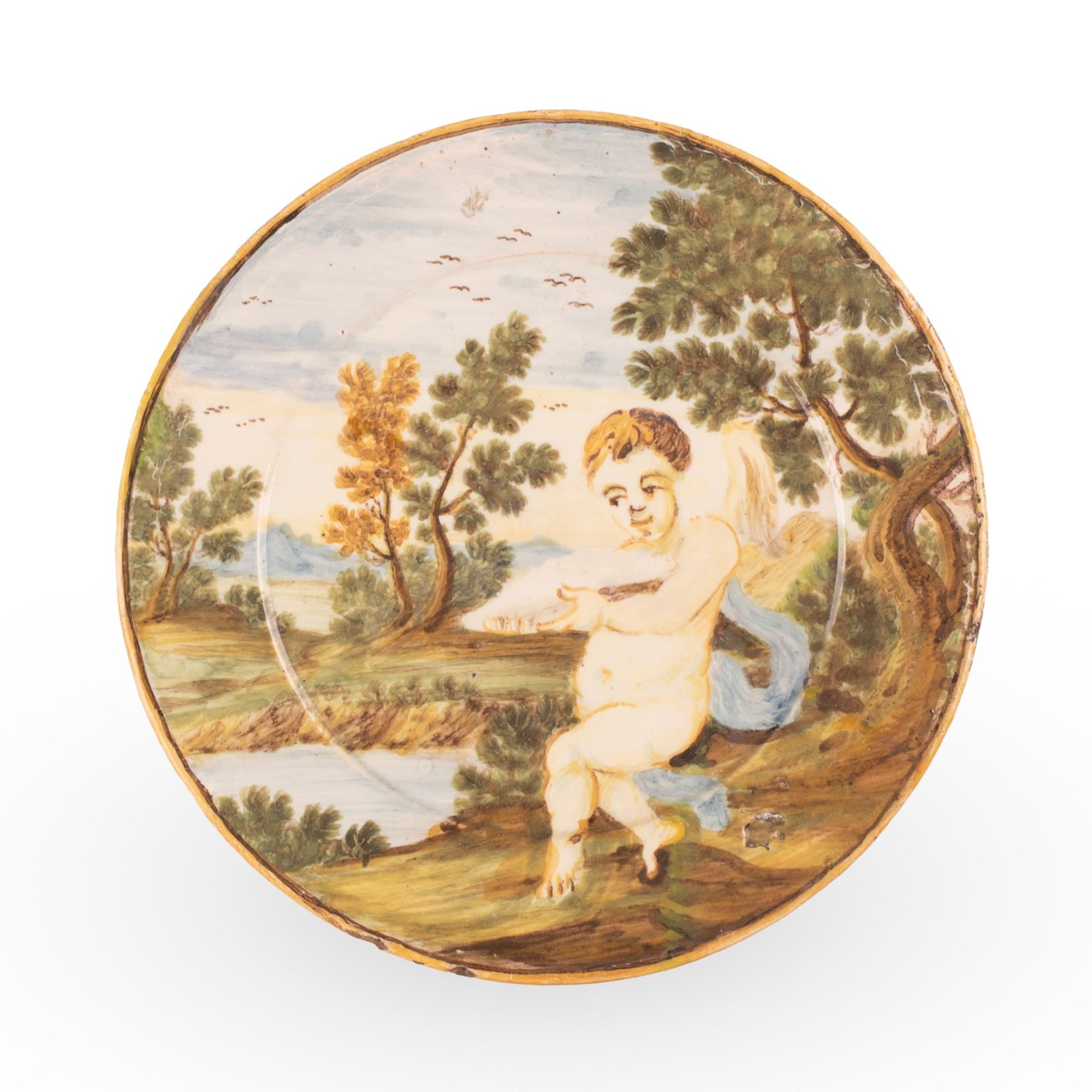 Piattino in maiolica decorato in policromia con paesaggio alberato e putto in primo piano. 