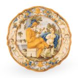 Piatto in maiolica decorato al cavetto con scena istoriata di fumatore di pipa e putto.