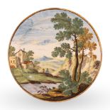 Piatto in maiolica decorato in policromia con paesaggio alberato, fiume, personaggi e case