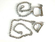 Two single Hiatt cuffs/shackles, in different sizes, attached to long metal chains, the keys stamped