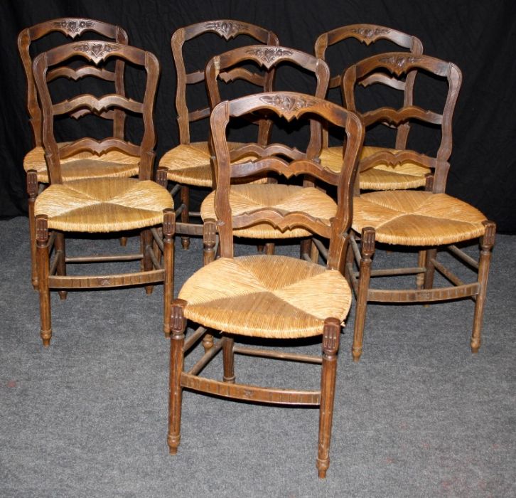 A set of seven late 19th century French provincial oak ladder back dining chairs, each with florally