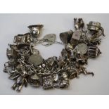 A sterling silver and white metal charm bracelet with numerous charms and padlock clasp, 182.6g (6.