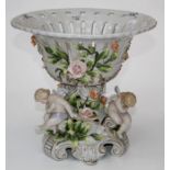 A Dresden style porcelain large compote decorated with putti and pendant roses raised on scroll