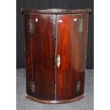 An early 19th century mahogany barrel fronted hanging corner cupboard with pierced brass escutcheon,