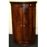 A late George III figural mahogany convex hanging corner cupboard enclosed by a pair of panel
