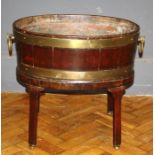 A George III mahogany and brass band oval open wine cooler, having ring handles and raised on square