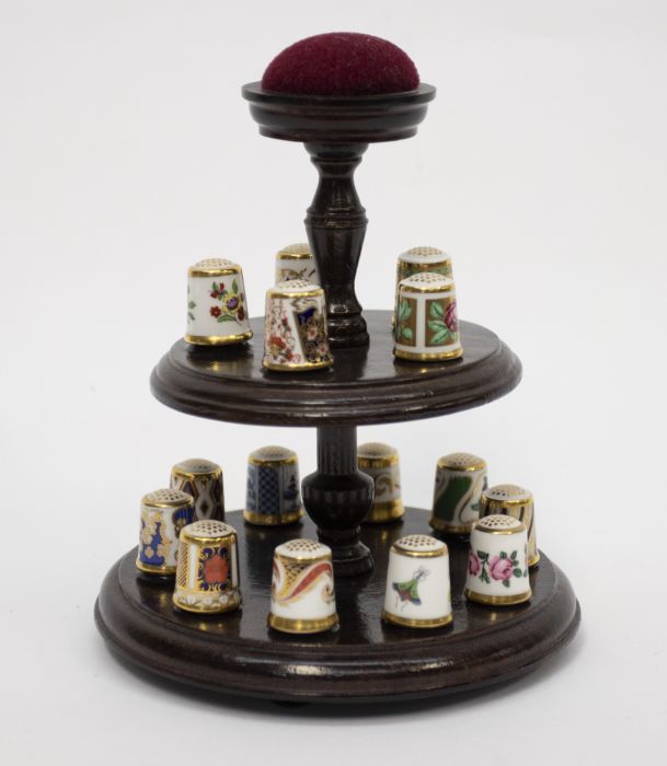 A collection of 15 Royal Crown Derby thimbles on a wooden display case stand with a pin cushion (all