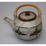 Manner of Bernard Leach, a stoneware studio pottery teapot and cover, with cane handle, decorated
