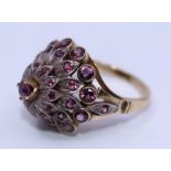 A 14ct. yellow gold and ruby dress ring, the domed white metal head claw set central round cut