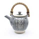 John Gibson (Courtyard Pottery) teapot on grey ground with floral decoration and cane handle. Height
