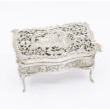 An Edwardian silver large dressing table box cast as a serpentine table on scroll legs, the cover