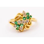 An emerald and diamond cluster ring, scrolled gold wire work inset with two floral claw set clusters