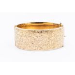 A 9ct gold hinged bangle, scroll and foliate decoration to the top, width approx 25mm, internal