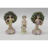 A pair of Derby style standing Putti, each holding a basket of flowers, with tree and floral