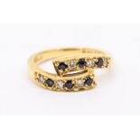 A diamond and sapphire 18ct gold cross over ring, the top with curved cross over set with