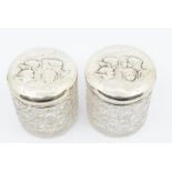 A pair of Edwardian cut glass circular large silver mounted toilet bottles, the covers chased with