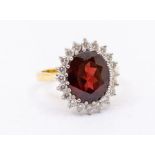 A garnet and diamond 18ct gold cluster ring, comprising a large oval cut garnet to the centre approx