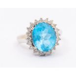 A blue topaz and diamond cluster ring, comprising a oval cut blue topaz within a border of claw