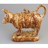 A mid-nineteenth century treacle glaze cow creamer and lid, c. 1840-50. 20 cm long (1) Condition: