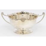 A George VI silver two handled bowl, scroll border with rocaille decoration, geometric handles,