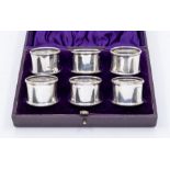 A matched set of six George V silver napkin rings, with ribbon tied reeded borders, in fitted