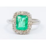 An emerald and diamond 18ct white gold cluster ring, comprising an emerald cut to the centre