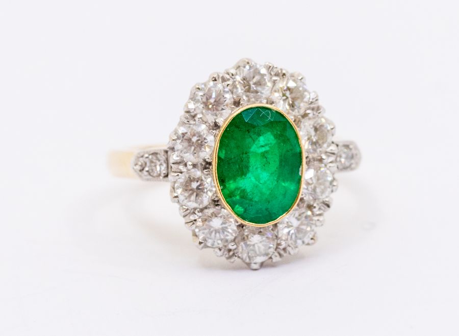An emerald and diamond 18ct gold  cluster ring, comprising an oval cut emerald to the centre, rub