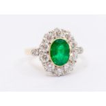 An emerald and diamond 18ct gold  cluster ring, comprising an oval cut emerald to the centre, rub