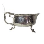 an arts and crafts silver milk jug with hammered decoration and hoof feet, handle intertwined with a