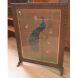An early 20th Century oak fire screen with woolwork peacock detail