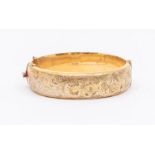 A 9ct gold hinged bangle with engraved scrolled decoration, width approx 15mm, internal diameter
