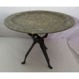 A folding African table with a brass top, 39cm high x 57cm diameter