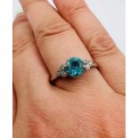 An Art Deco style ring, set with a blue zircon and six white, old cut stones. Size Q. In white