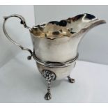 An Irish silver scallop edge cream jug with claw feet, drawn from lions head decoration, with
