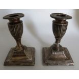 A pair of sterling silver weighted candlesticks in the form of a classical urn on a square foot.