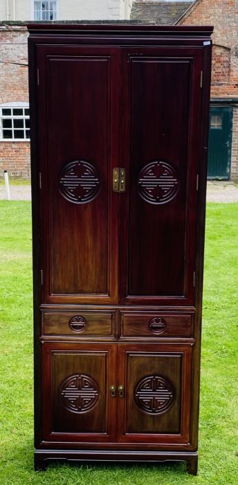 A Chinese hardwood cabinet, the upper section with moulded cornice above a pair of doors with carved