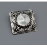 An Arts and Crafts brooch in a square shape and set with a mabe pearl/mother of pearl, bezel set