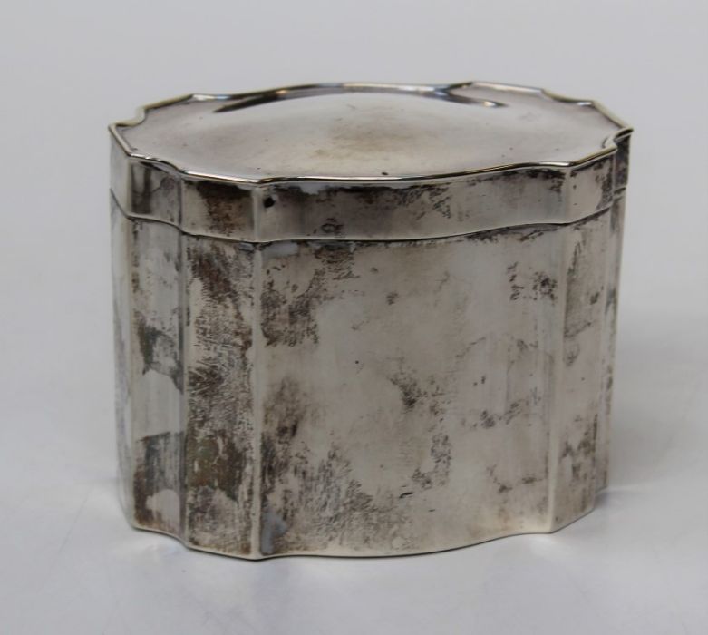 A George V silver tea caddy of re-entrant oval form, with hinged cover and gilded interior.