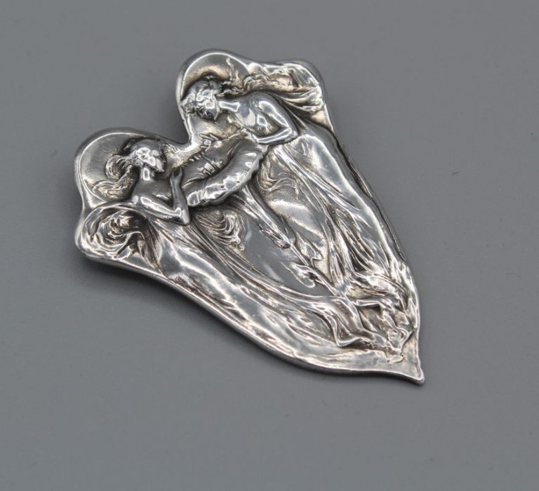 An unmarked white metal Art Nouveau style brooch depicting two nymphs/fairies peering into an open