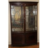 A 19th century mahogany vitrine of bow front form, the dentil cornice over a pair of astragal glazed