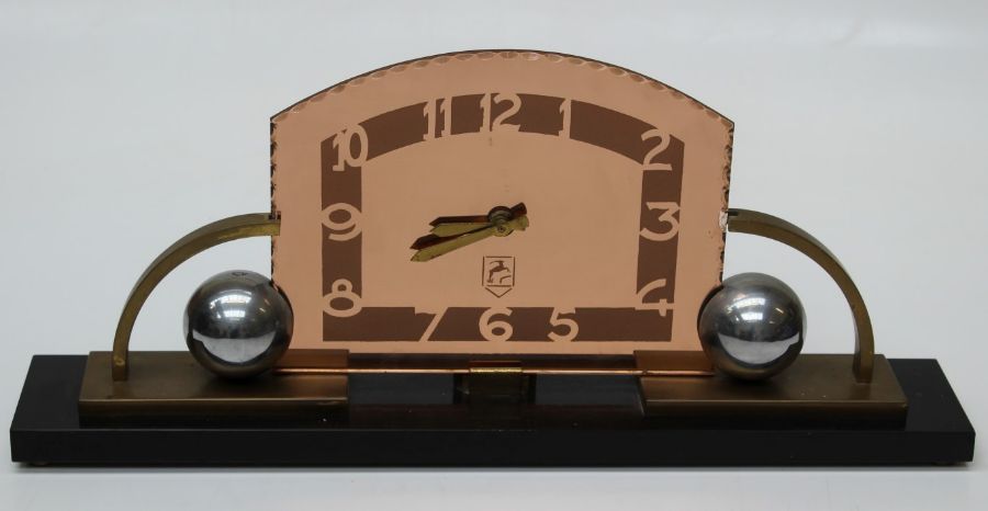 An Art Deco mantle timepiece, the narrow oblong slate base having a pink glass stylized frame with a