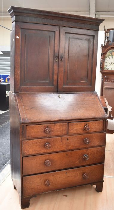 George III oak bureau/bookcase with panelled doors above a drop-down writing top. It has a