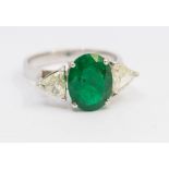 An emerald and diamond three stone 18ct white gold ring, comprising a central oval mixed cut
