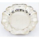 A George V silver floral shaped bowl with raised border, on four scroll feet, hallmarked by Thomas