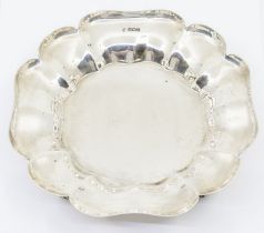 A George V silver floral shaped bowl with raised border, on four scroll feet, hallmarked by Thomas