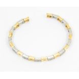 A diamond set two tone 18ct gold torque bangle, comprising concave squared open links, alternating