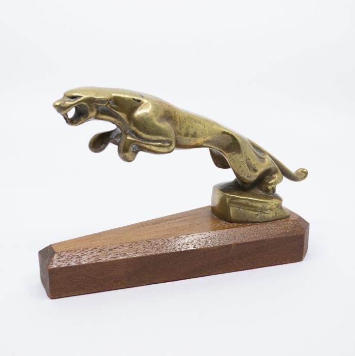 A brass car mascot modelled as a leaping Jaguar on a wooden plinth. Height approx 12.5cm, length